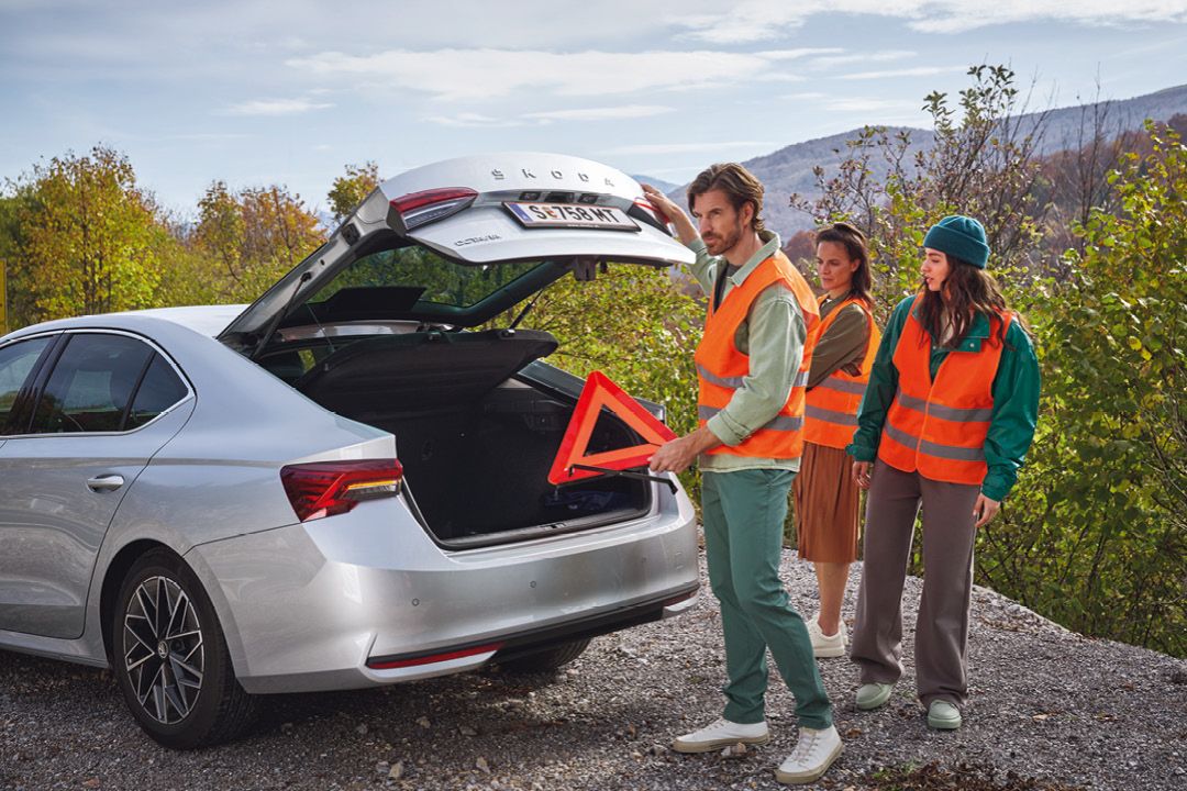 Ein Mann in Warnweste nimmt ein Warndreieck aus dem Kofferraum eines Škoda Octavia. Eine Frau in Warnweste steht neben ihm.