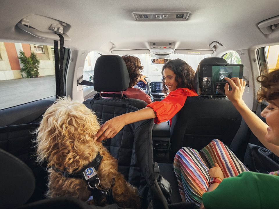 Vier Personen und ein Hund sitzen in einem Škoda. Ein Kind zeigt auf ein Tablet, das an der Rückenlehne des Vordersitzes befestigt ist. Der Hund sitzt auf dem Rücksitz und trägt ein Geschirr.