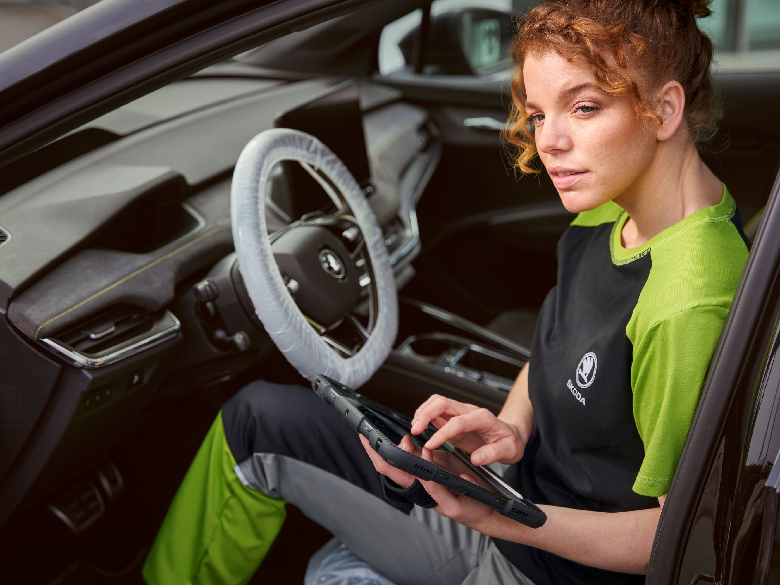 Eine Škoda Mechanikerin sitzt in einem Škoda und tippt in ihr Tablet.