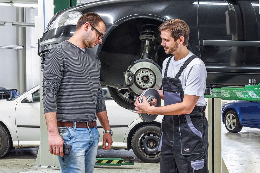 Ein Škoda Mechaniker in der Werkstatt zeigt einem Kunden die Bremsscheiben