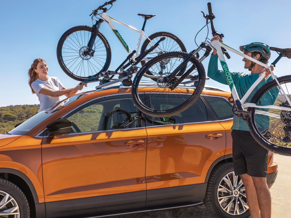 Zwei Personen befestigen Fahrräder auf dem Dach eines orangefarbenen Škoda.
