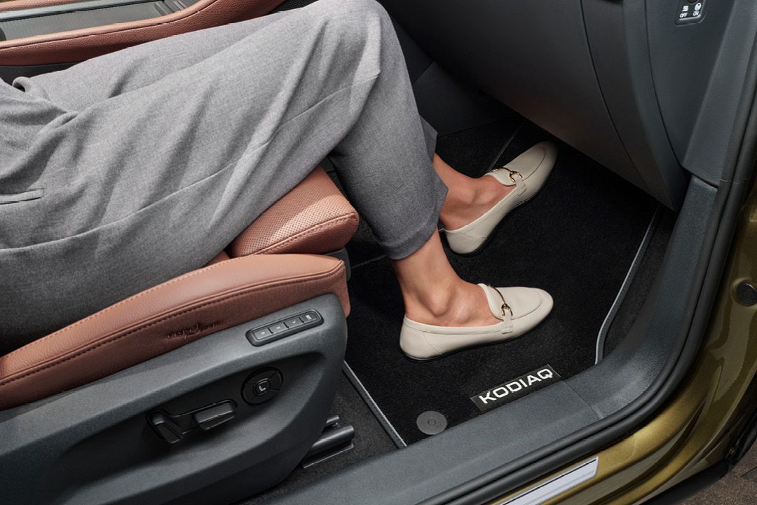 Eine Person sitzt in einem Škoda Kodiaq und hat ihre Beine auf einer Textilfußmatte mit Kodiaq Schriftzug platziert.