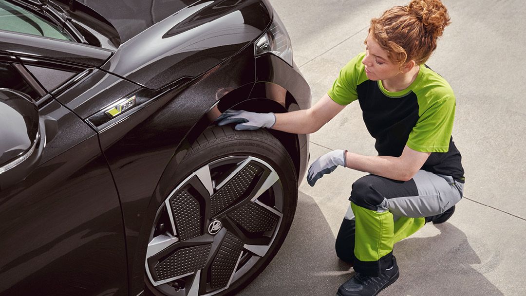 Eine Škoda Mechanikerin kontrolliert die Reifen von einem Škoda Enyaq.