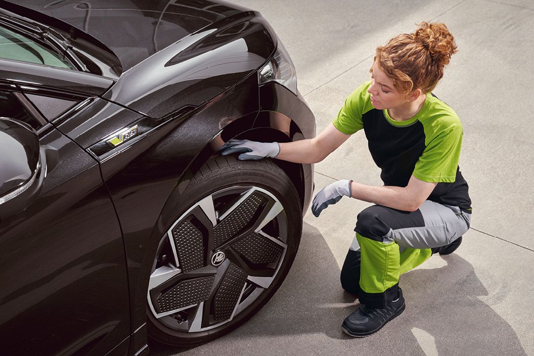 Eine Škoda Mechanikerin kontrolliert die Reifen von einem Škoda Enyaq.