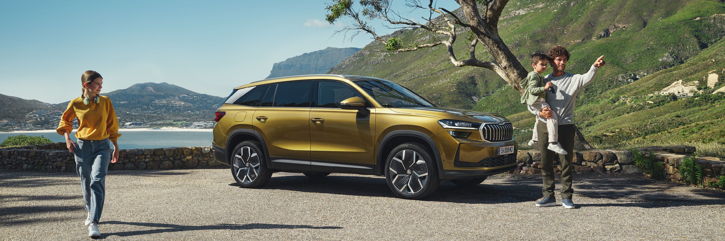 Ein Škoda Kodiaq unter einem Baum an der Meeresküste. Eine Familie steht vor dem Fahrzeug.