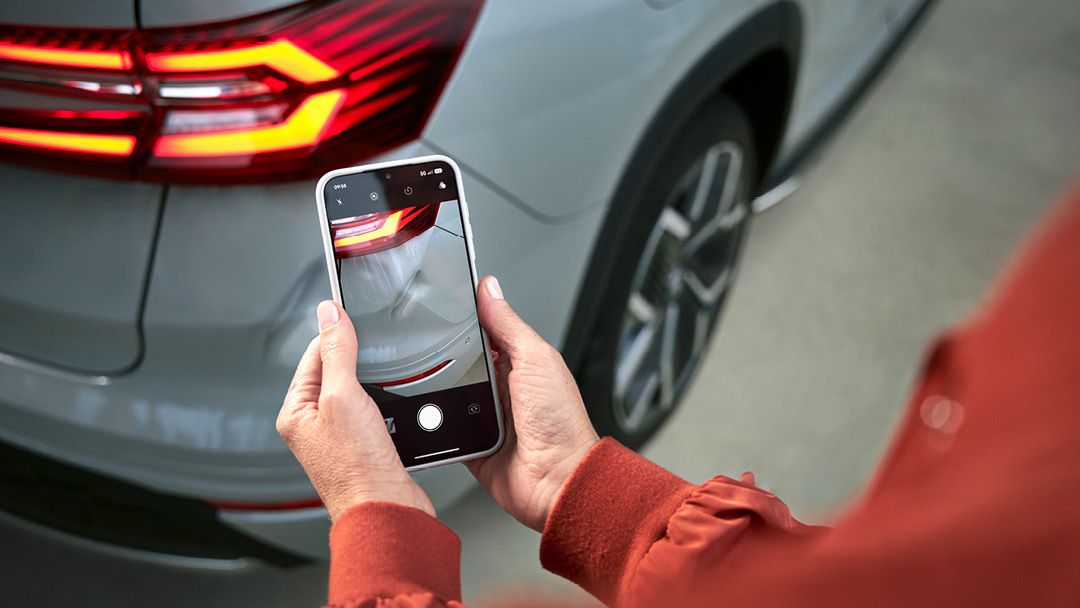 Zwei Hände halten ein Smartphone und fotografieren einen Lackschaden bei einem Škoda.