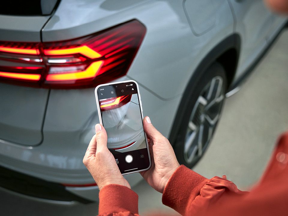 Zwei Hände halten ein Smartphone und fotografieren einen Lackschaden bei einem Škoda.