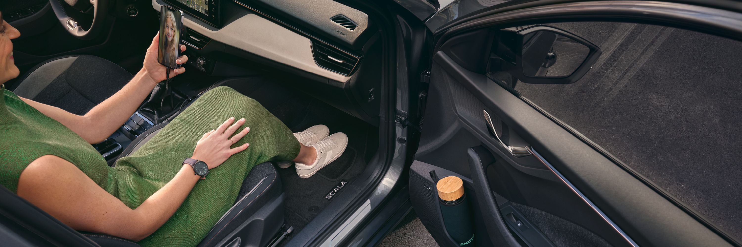 Eine Frau in einem Škoda Scala blickt auf ihr Smartphone