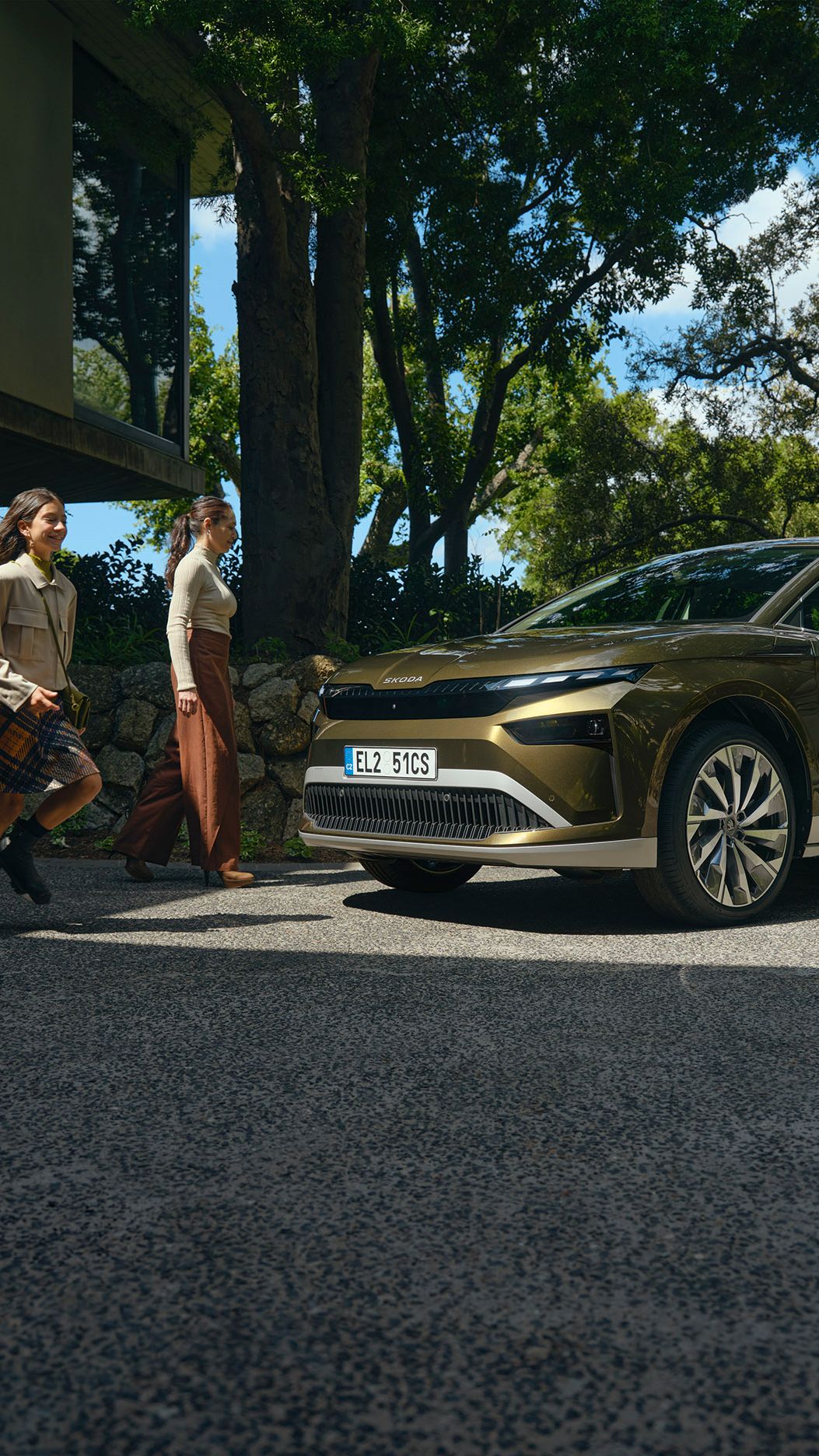 Eine Familie steht auf einem Parkplatz neben einem Haus und sie gehen auf einen grünen Škoda Enyaq zu