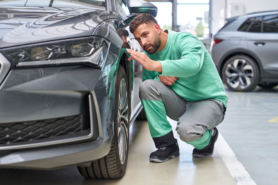 Ein Škoda Mechaniker kontrolliert den Lack bei einem grauen Škoda.