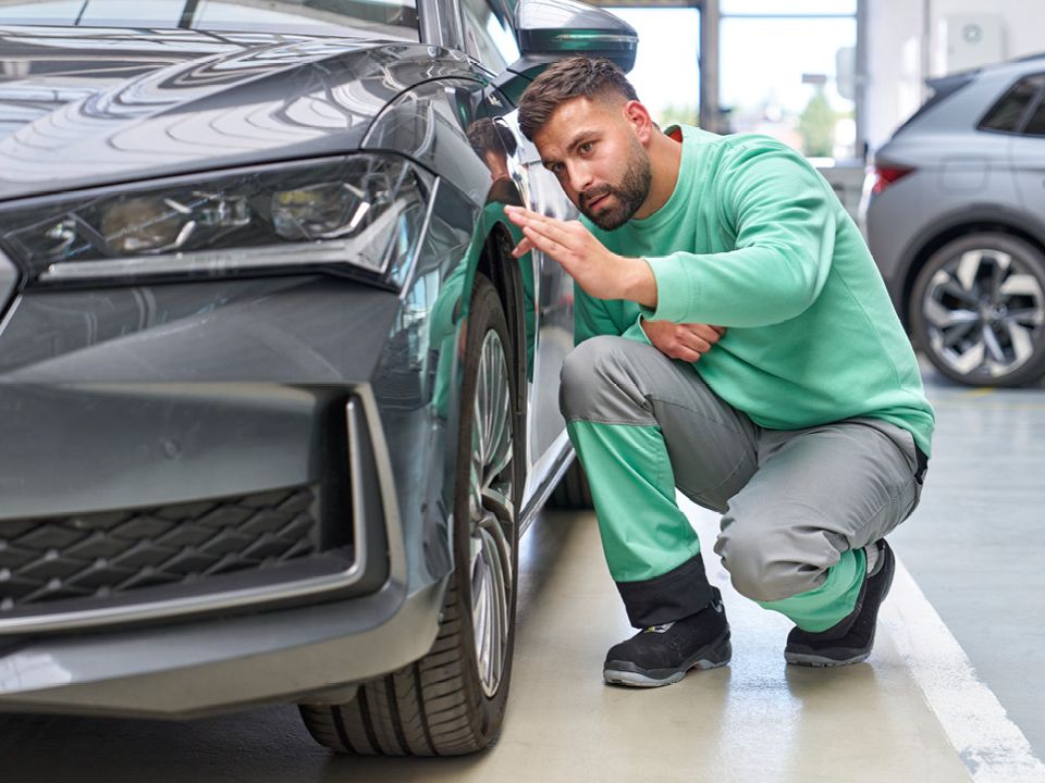 Ein Škoda Mechaniker kontrolliert den Lack bei einem grauen Škoda.