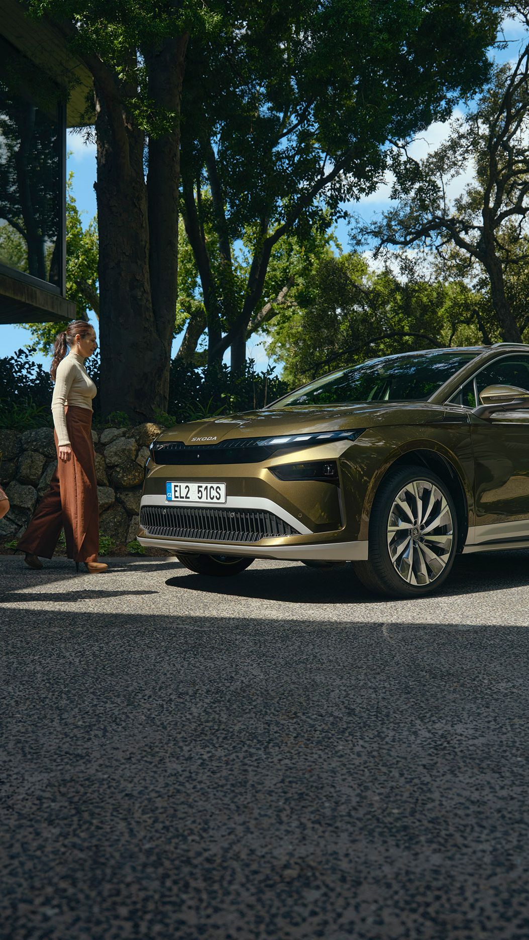 Eine Familie steht auf einem Parkplatz neben einem Haus und sie gehen auf einen grünen Škoda Enyaq zu