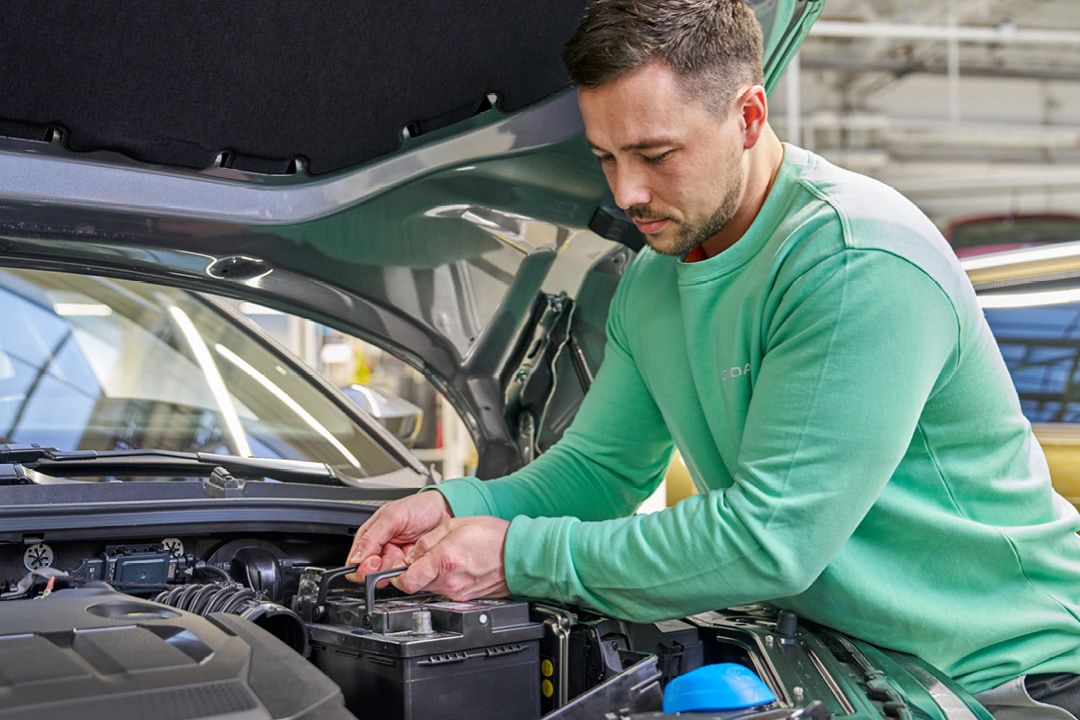Ein Škoda Mechaniker wechselt eine Starterbatterie.