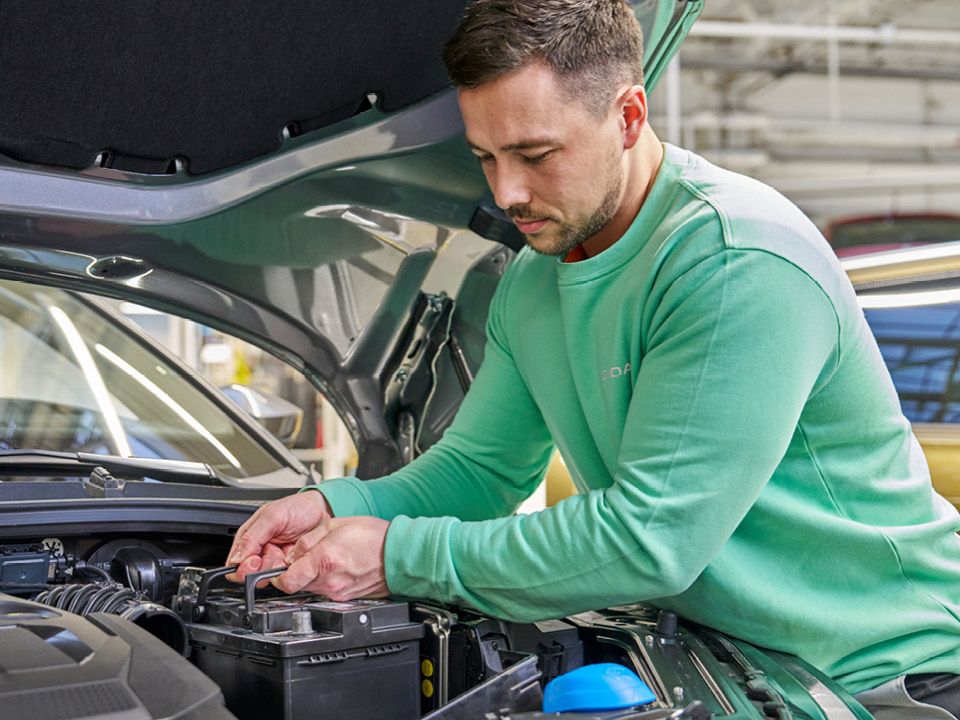 Ein Škoda Mechaniker wechselt eine Starterbatterie.